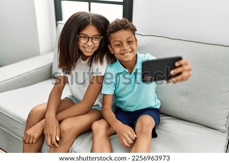 Brother and sister make selfie by the smartphone sitting on sofa at home