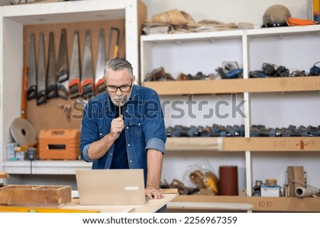 Portrait of positive professional caucasian man carpenter standing in furniture repair shop working with laptop.