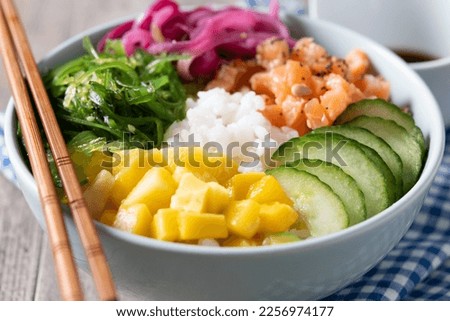 Poke bowl with rice, salmon,cucumber,mango,onion,wakame salad, poppy seeds ands sunflowers seeds on wooden background