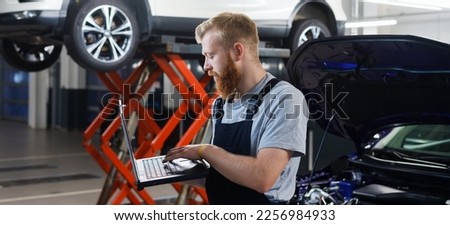 An auto mechanic engineer stands with a professional diagnostic laptop against the background of a service station. Diagnosis of vehicle errors . Panoramic photography