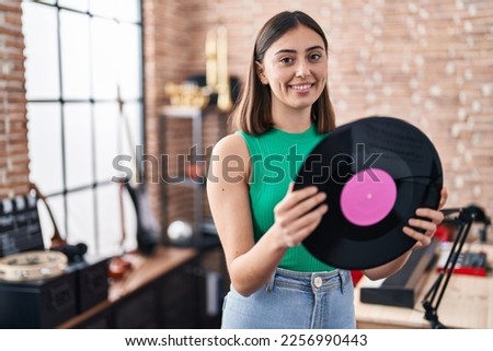 Young hispanic woman musician holding vinyl disc at music studio