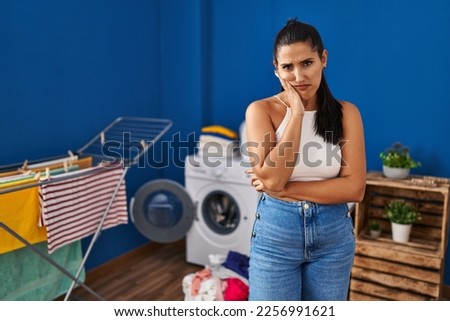 Young hispanic woman at laundry room thinking looking tired and bored with depression problems with crossed arms. 