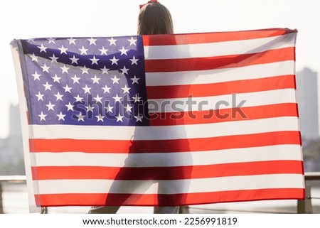 Patriotic holiday. Happy young stylish caucasian woman with American flag outdoors on sunset. USA celebrate independence day 4th of July.