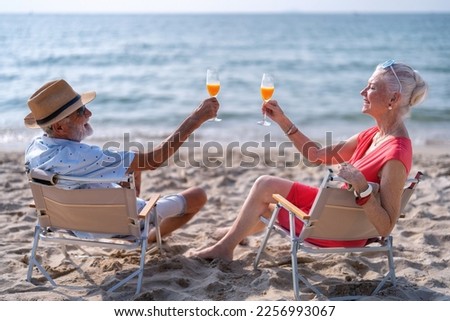 Couple old mature people on the sand at the beach sitting enjoying drink juice and living the moment Royalty-Free Stock Photo #2256993067