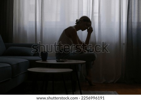 Young depressed woman sitting on the sofa next to the window	 Royalty-Free Stock Photo #2256996191