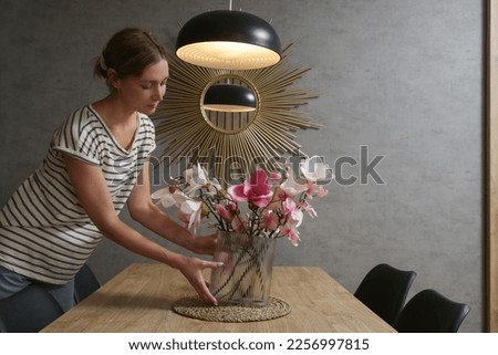 Woman arranging vase with flowers on table. Housewife taking care of coziness in apartment. Interior decor, household and home improvement concept. Royalty-Free Stock Photo #2256997815