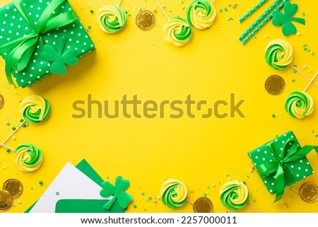 Saint Patrick's Day concept. Top view photo of green gift boxes meringue candies sprinkles gold coins envelope with card straws clovers on isolated vivid yellow background with copyspace in the middle