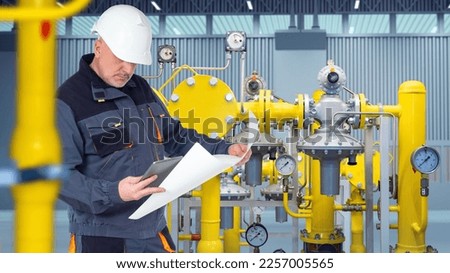 Master in setting up oil and gas equipment. Man near compressor station. Specialist with tablet and papers is standing in hangar. Man is gas equipment repairman. Guy controls gas supply of factory