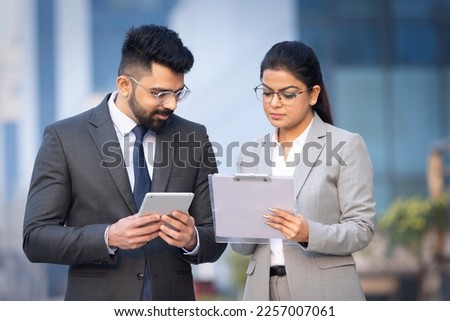 Indian businessman and businesswoman using digital tablet on city street.