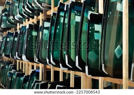 Lots of windshields for different cars on service station shelves ready to install or replace broken glass with cars. Royalty-Free Stock Photo #2257008543