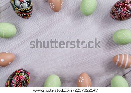 colorful easter eggs arranged on light wood around the picture with a blank space in the middle