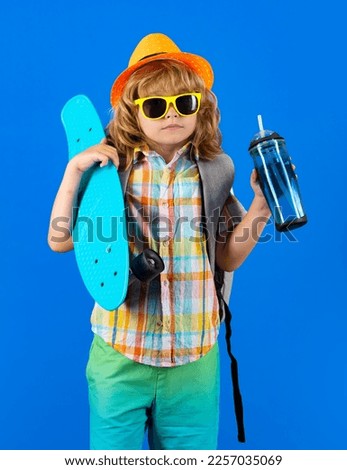 Childhood. Cute child with skateboard and water bottle on color isoalted background. Funny kid boy, stylish skater holding skateboard in studio.