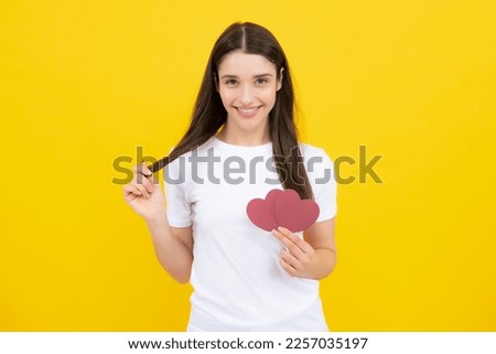Valentines Day. Beautiful young woman with heart in her hands. Attractive woman with paper heart over yellow background.