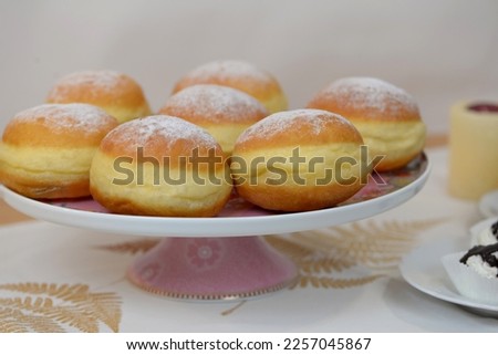Plate with home baked berliner doughnuts with meringue cakes and candle in background. Traditional carnival food: fluffy donuts made of rich sweet dough, stuffed with jam, sprinkled with sugar powder. Royalty-Free Stock Photo #2257045867