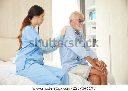 nurse or caregiver using stethoscope to examine senior man at home