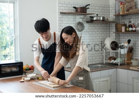 Asian couple standing in kitchen at home preparing together yummy dinner on first dating, spouses chatting enjoy warm conversation and cooking.