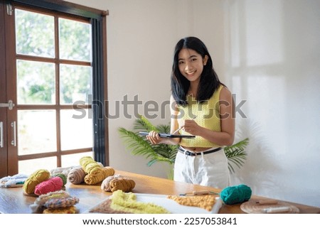 Designer Asian Woman holding digital tablet creative for handmade Punch needle in studio workshop. designer workplace craft project DIY embroidery concept.