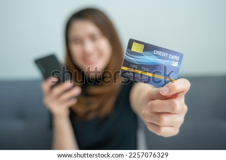 Asian woman showing her credit card for shopping online on mobile phone applications. A credit card is a type of credit facility, provided by banks that allow customers to borrow funds.
