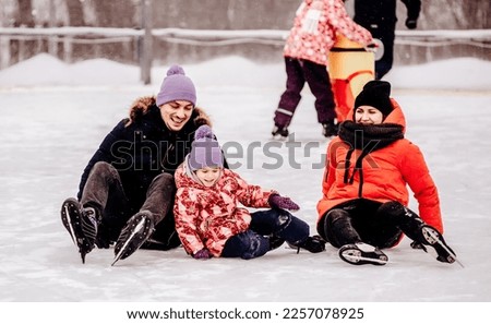Happy family spending time together at outdoor ice skating rink. falling on the skating rink