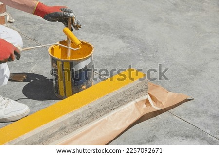 Professional painter at work. Unrecognizable young man uses a paint roller to apply special acrylic paint for road marking on a curb of a parking lot.