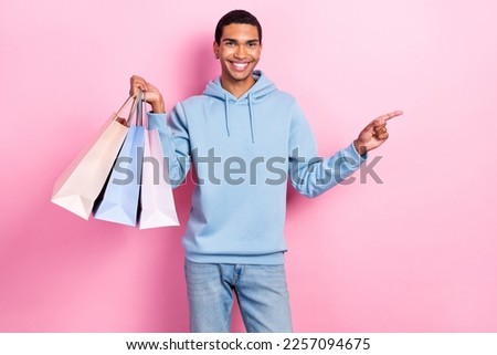 Photo of cheerful good mood student man hold much packages from shopping center direct finger empty space prices isolated on pink color background