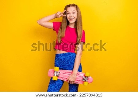 Photo of optimistic cheerful schoolgirl straight hairdo pink t-shirt showing v-sign hold skateboard isolated on yellow color background