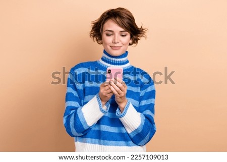 Photo of cute woman hold smartphone remote fast wifi connection reading digital ebook wear blue striped turtleneck isolated on beige color background