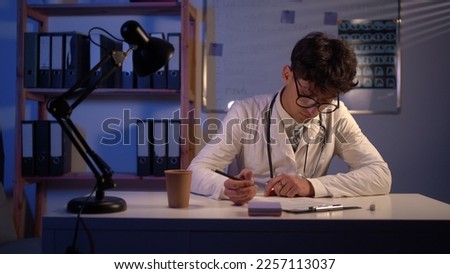 Young arab doctor sitting at table and writing on a document report in hospital office. Medical healthcare staff and doctor service concept.
