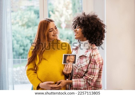 Couple of women presenting the pregnancy photo proud of their future. Concept: maternity, pride, integration Royalty-Free Stock Photo #2257113805