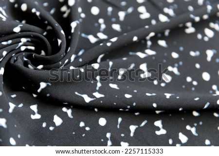 Abstract pattern of white spots on black fabric with folds as background