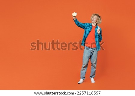 Full body young blond man wear blue shirt orange t-shirt doing selfie shot on mobile cell phone post photo on social network isolated on plain red background studio portrait. People lifestyle concept