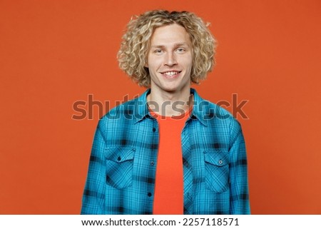 Young smiling cheerful positive optimist fun happy cool blond caucasian man wearing blue shirt orange t-shirt looking camera isolated on plain red background studio portrait. People lifestyle concept