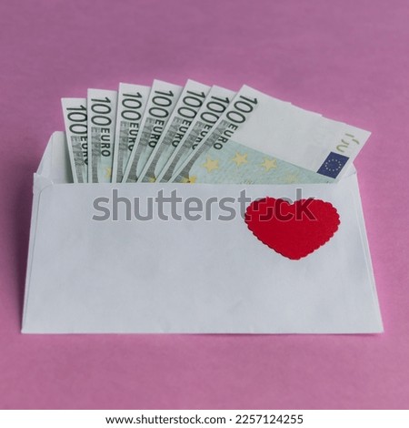 Paper envelope with 100 euro banknotes and a red heart on a pink background. Banknotes stick out from the envelope. Conceptual gift for Valentine's Day, wedding, birthday. Close-up