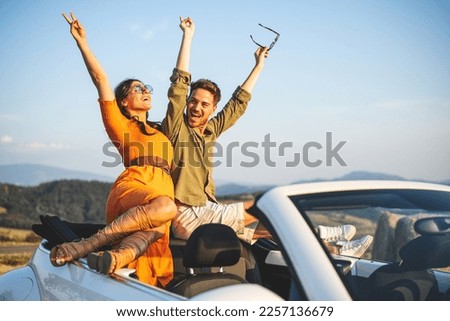 Sunset sun bath for a couple of lovers on the go, travel and holiday lifestyle. young couple having fun standing on convertible car, countryside background Royalty-Free Stock Photo #2257136679