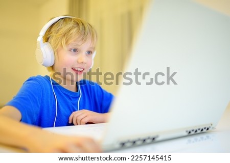 A boy in headphones plays a computer game or chats with a friend in a messenger. Child and gadgets. Kids using modern technology. Online education and entertainment for children.