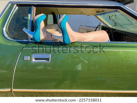 Teal blue high heels, with silver and cheetah print , sticking out of a green vintage car