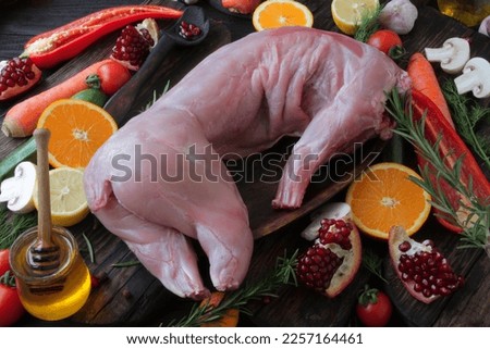 The carcass of a raw, fresh rabbit on a wooden table in a wooden plate, around the rabbit are ingredients for marinade and vegetables, spices, herbs for baking.