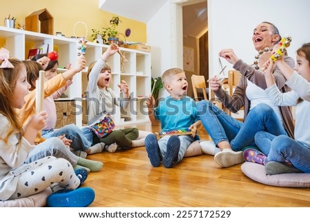 Kindergarten teacher with children sitting on the floor having music class, using various instruments and percussion. Early music education Royalty-Free Stock Photo #2257172529