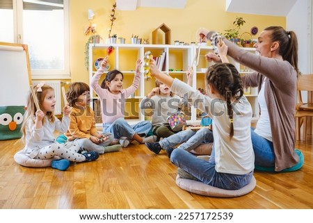 Kindergarten teacher with children sitting on the floor having music class, using various instruments and percussion. Early music education Royalty-Free Stock Photo #2257172539