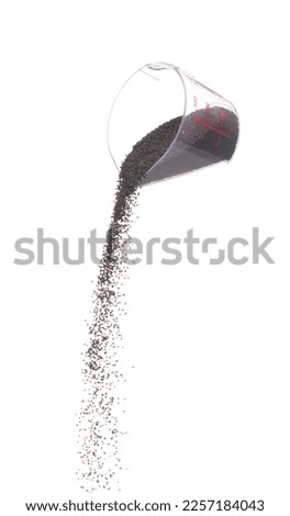 Black Sesame pouring down from measure cup, black Sesame grain wave floating, fall in air. Basil seed is organic healthy food. White background Isolated high speed shutter, freeze stop motion