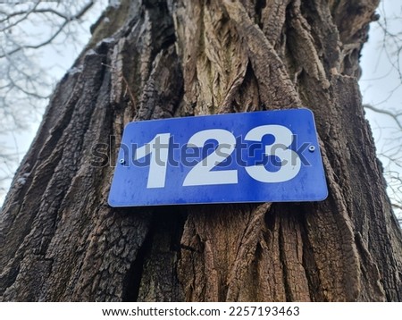 A 123 civic number attached to the trunk of a tree.
