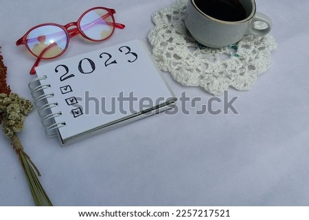 New year resolutions 2023 on desk. 2023 resolutions list with notebook, coffee cup on white background. Goals, resolutions, plan, action, checklist concept. New Year 2023 template, copy space.