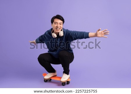Image of young Asian man playing skateboard on purple background Royalty-Free Stock Photo #2257225755
