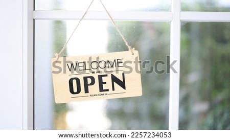 Open, WELCOME wooden sign board hanging on the glass door, A business sign that says ‘Open’ on cafe or restaurant hang on door at entrance. Clear color tone style.