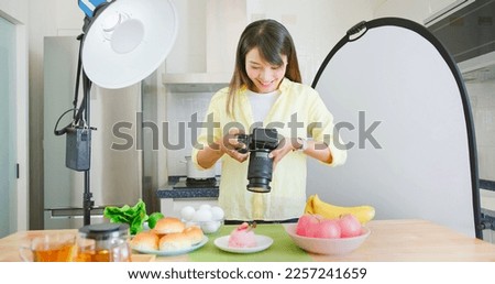 asian female photographer is using digital camera to take pictures in kitchen and she satisfied with the work