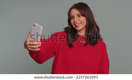 Pretty young woman influencer blogger taking selfie on smartphone, communicating video call online, recording new social media vlog story for subscribers. Girl isolated on gray studio background