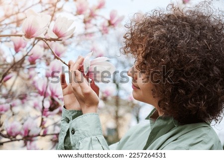 Teenager girl enjoy the smell and beauty of blooming magnolia flowers. Large flowering bush in the spring park. Springtime, mental health, no allergy