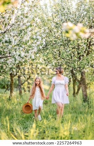 Mom and daughter are walking in the spring garden. Family walk through the blooming garden