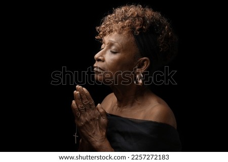 Beautiful elderly 70+ year old Christian African American black woman religiously and fervently praying to God with eyes closed and hands together holding a cross Royalty-Free Stock Photo #2257272183
