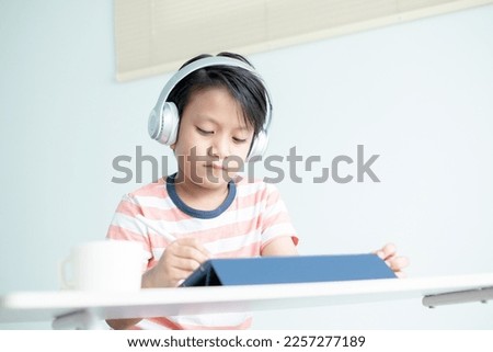 Asian boy kid with headphones is drawing pictures and writing on the digital tablet using digital pencil